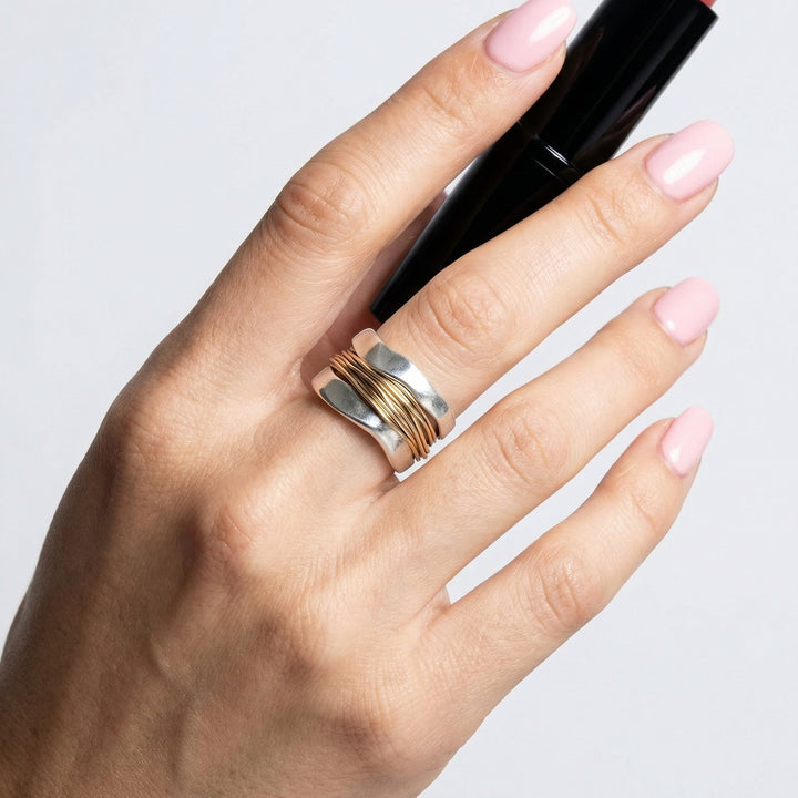 Nahaufnahme: Damen Silberring im Wickeldesign, goldene Akzente. Hochwertiger Schmuck, eleganter Fingerschmuck.