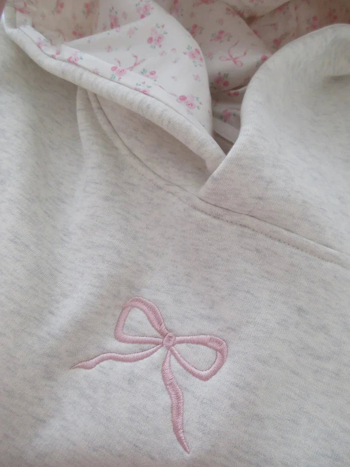 Gemütlicher Elfenbein Damen Hoodie mit Kängurutasche & Kapuze, verziert mit femininen rosa Schleifen.