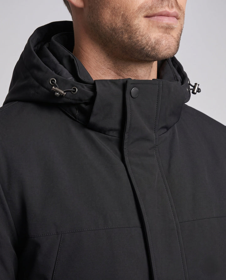 Mann trägt thermische Herren Softshell-Winterjacke mit Kapuze beim Wandern im Schnee.
