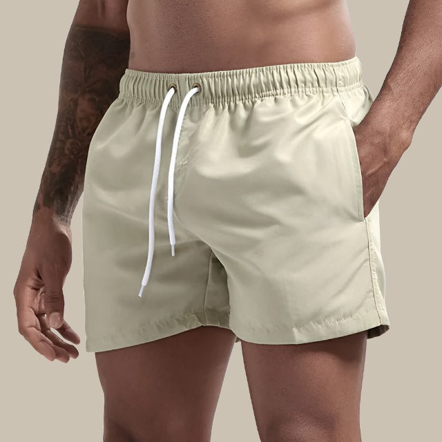 Mann in Slim Fit Badeshorts beim Spaziergang am Strand, ideal für sommerliche Wasseraktivitäten.